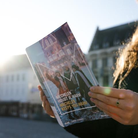 Vrouw met herfst-en winterbrochure in de hand. Je ziet de cover van de brochure. Zonneschijn op de achtergrond.