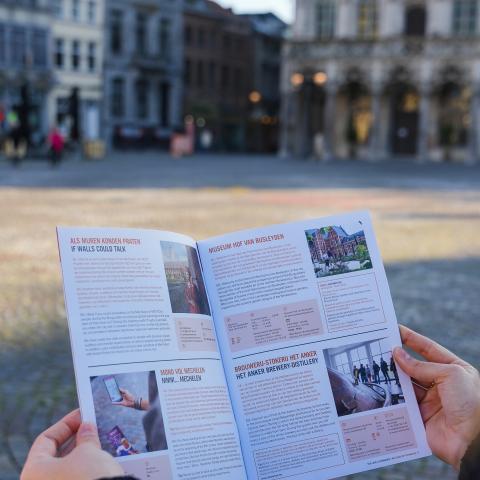 Vrouw met herfst-en winterbrochure in de hand. Je ziet de binnenkant van de brochure. Stadhuis op de achtergrond.